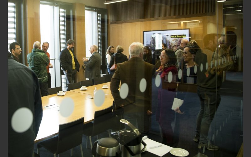 photograph through a window of a group of meeting standing in a meeting room