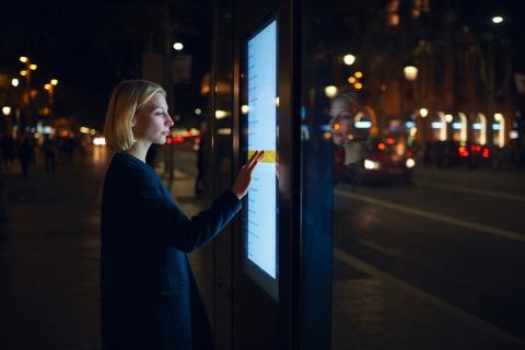 Woman using public touch screen display in city at night