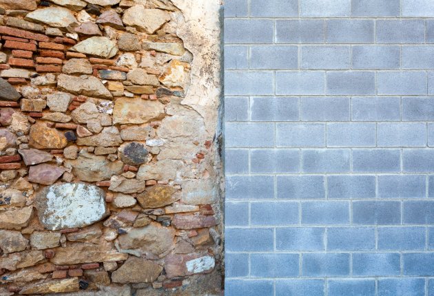 Photo of a wall divided in two. The left side is chaotically made of rocks and thin red bricks. The right is orderly grey concrete bricks.