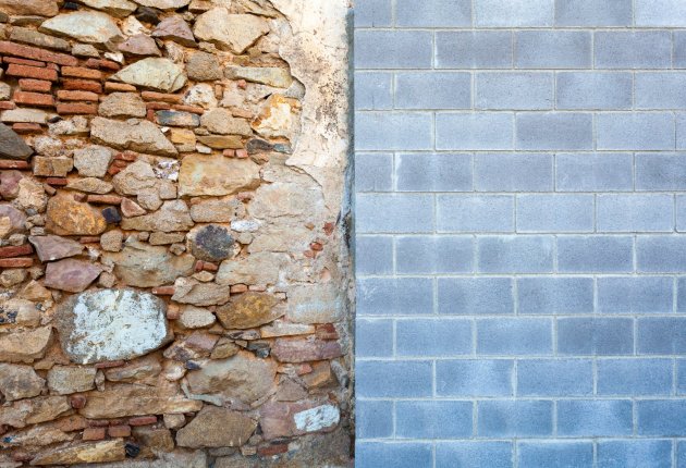 An old wall meets a new one - shutterstock Photo of a wall divided in two. The left side is chaotically made of rocks and thin red bricks. The right is orderly grey concrete bricks.