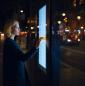 Woman using public touch screen display in city at night