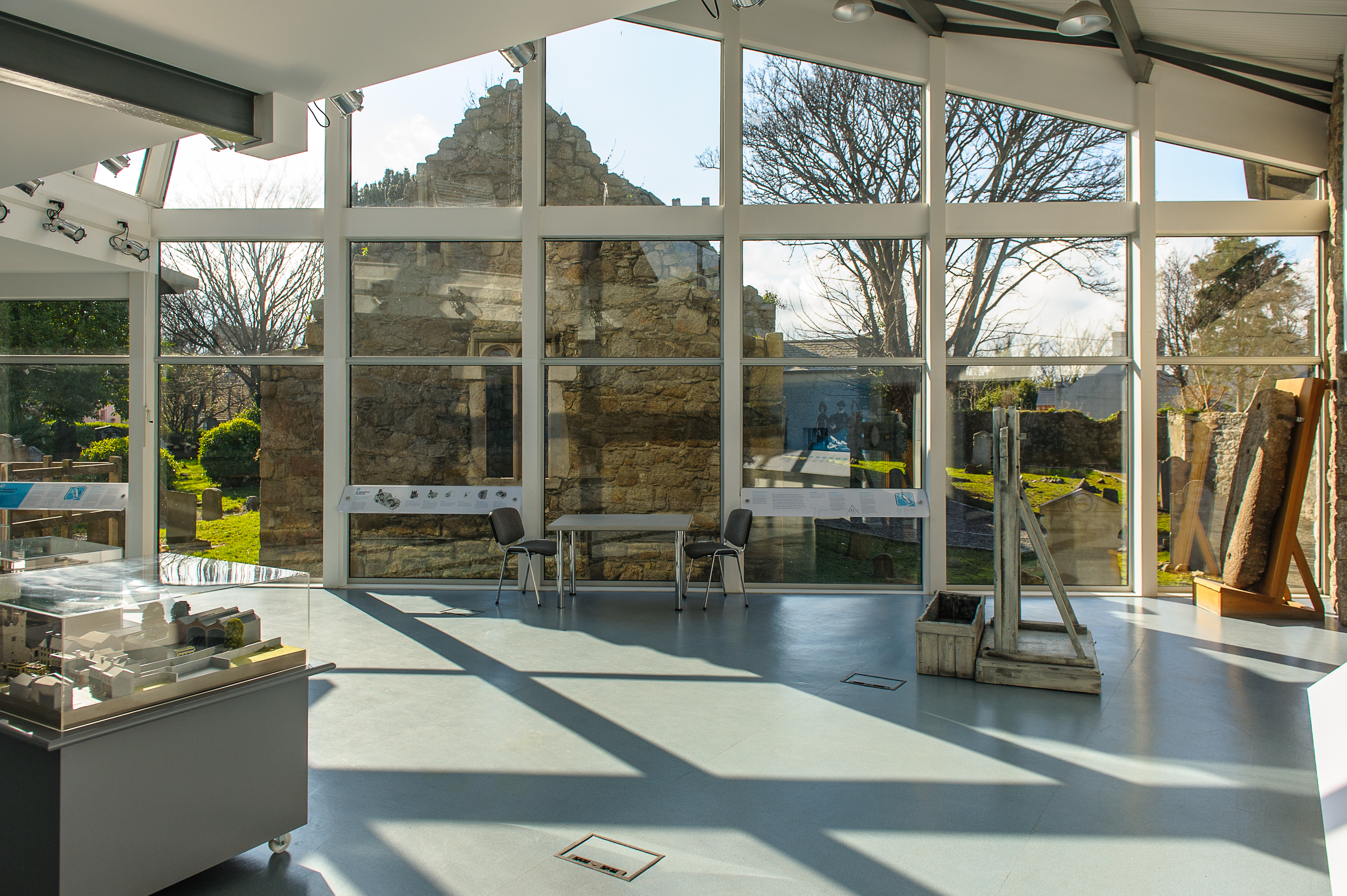 view from the interior of a modern building with full length glass windows out to the ruins of a church and a graveyard