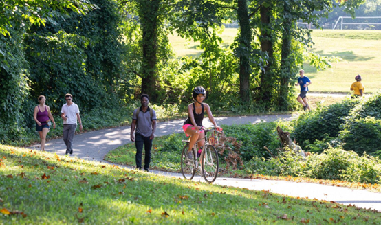 adult and kids cycling, some running,some walking on a pathway through a park