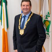 man standing in front of Irish flag wearing chain of office