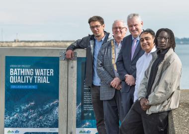 five men at bathing water quality trial kiosk with sea in background