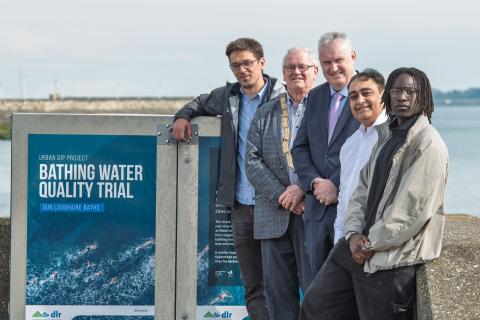 five men at bathing water quality trial kiosk with sea in background