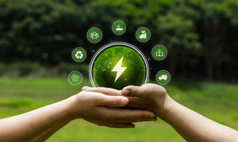 Hands holding a green sphere with an electricity symbol, surrounded by icons representing recycling, renewable energy, carbon reduction, sustainable industry, transport and community action.
