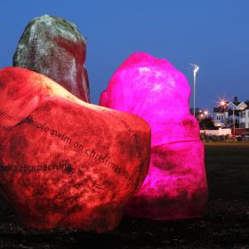 3 boulders are grouped together in a dark park. The boulders are glowing a range of pink colours