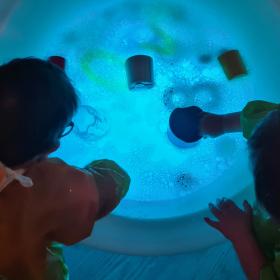 Two children leaning over a blue round pool of water with toys