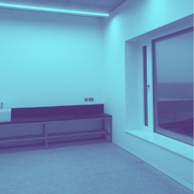 photo of the baths artist studio, tinted blue. it shows a sink and counter on the back wall and a large window to the right.