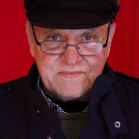 Photobooth Man Hat by Theresa Nanigian Man in black coat, hat and glasses in front of a red curtain