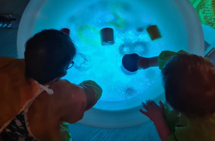 Two children leaning over a blue round pool of water with toys