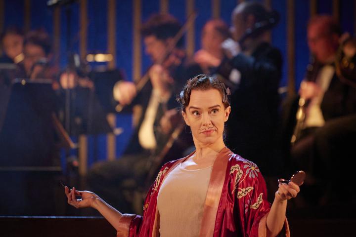Opera singer Sharon Carty on stage with a drawn-on moustache making a quizzical face