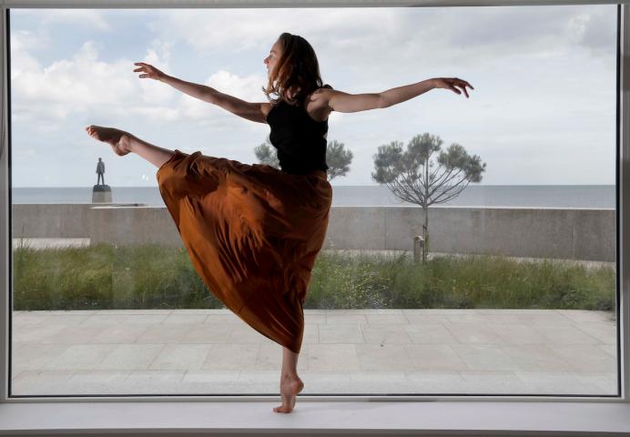 Dancer, Laura Sarah Dowdall kicking her leg and extending her arms with the sea in the background