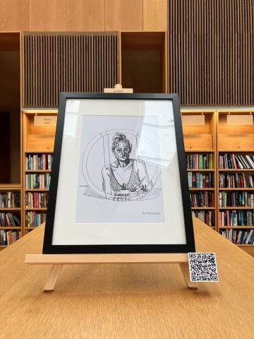 Self portrait drawing in a round mirror. drawing is in a black frame on an easel on top of a library bookshelf