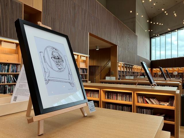 Self portrait drawing in a round mirror. drawing is in a black frame on an easel on top of a library bookshelf