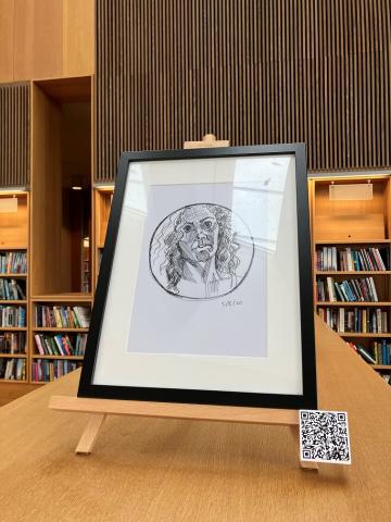 Self portrait drawing in a round mirror. drawing is in a black frame on an easel on top of a library bookshelf