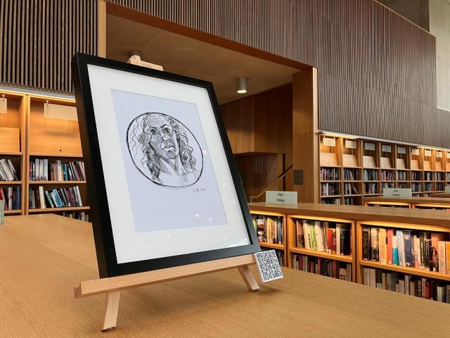 Self portrait drawing in a round mirror. drawing is in a black frame on an easel on top of a library bookshelf