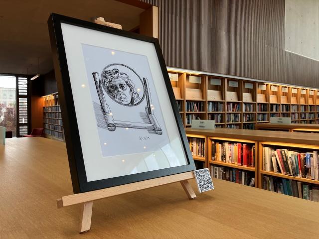 Self portrait drawing in a round mirror. drawing is in a black frame on an easel on top of a library bookshelf