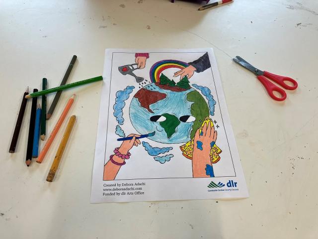 Colouring Sheet colouring pencils and a pair of scissors next to a coloured in drawing of planet earth with hands painting, cleaning and watering the earth