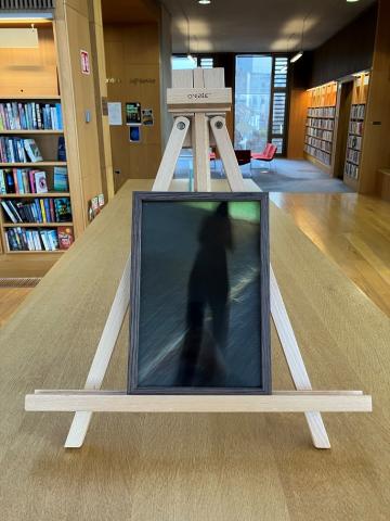A framed photo of a shadow in a a carpark at night is on an easel on top of a bookshelf in the Lexicon Library.