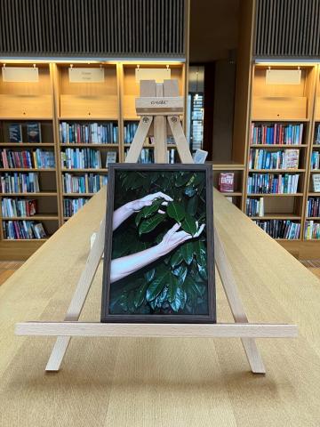 A framed photo of hands touching leaves is on an easel on top of a bookshelf in the Lexicon Library.