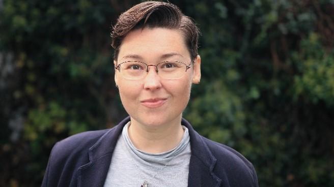 Anna Czarska is pictured in the centre of the frame, it is a head and shoulders photograph. Anna, who has short dark hair and wears glasses, is smiling