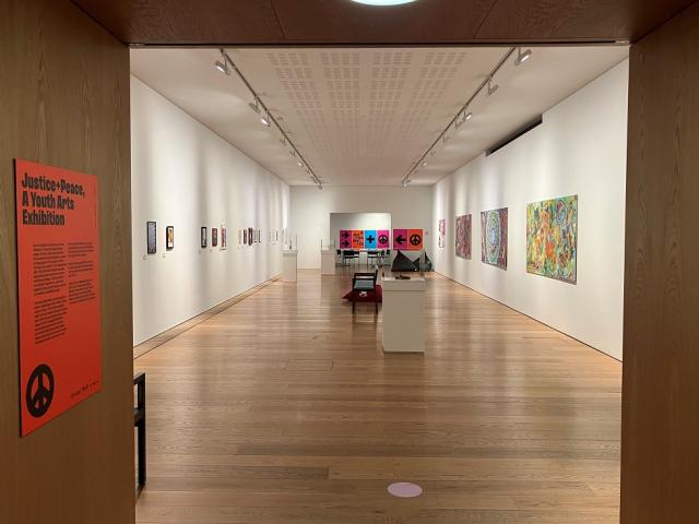 Looking through brown wood doors into the municipal gallery. It is a long room with colourful art on the walls and plinths with small sculptures