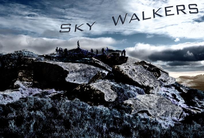 a rocky outcrop with scrub and grasses is in the foreground of this photograph. a number of people may be seen standing on the top of the rock in the distance, framed against a dramatic sky with clouds. The words Sky Walkers float in the clouds. The entire image is filtered with a blue tinged infra red filter.