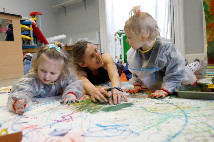 Artist Helen Barry with two early years children, drawing on a large white sheet of paper.
