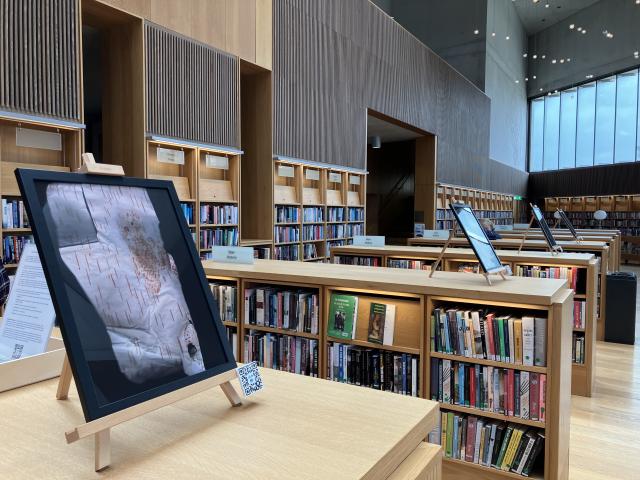 A view inside the lexicon library. 4 rows of chest height bookcases have framed artworks by Jonathan Brennan.