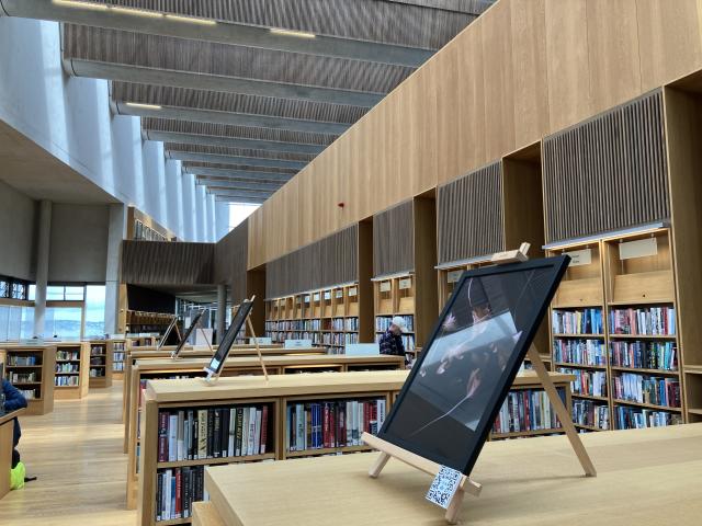 A view inside the lexicon library. 4 rows of chest height bookcases have framed artworks by Jonathan Brennan