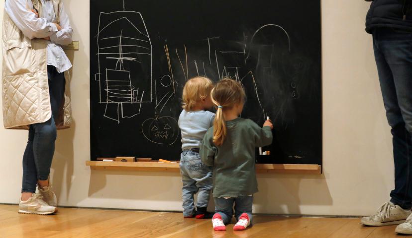 two small children are drawing on a blackboard while their grownups stand next to them