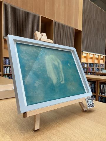 a fuzzy blue photograph, like from a vintage camera, shows a woman bending over with a towel draped over her head as if she is drying her hair after a swim