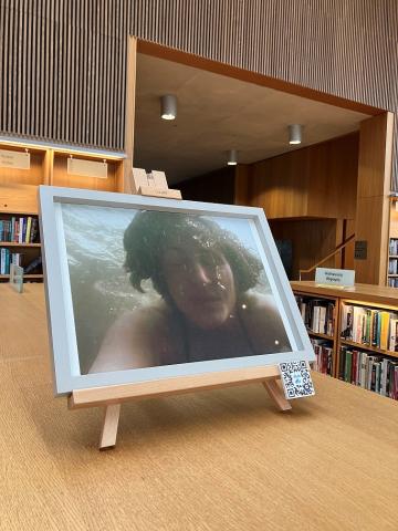 a framed photo on a chest height bookcase shows a woman's face under water with bubbles rising up from her mouth