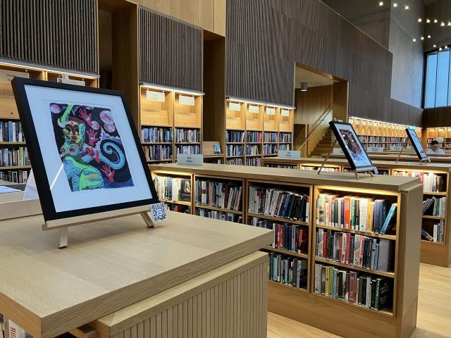 3 colourful framed artworks sit on top of 3 wooden chest height bookcases in the Lexicon Library