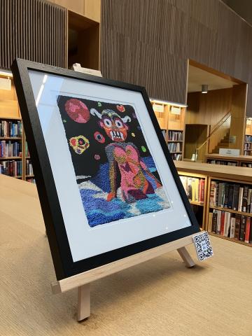 A colourful framed artwork sit on top of 3 wooden chest height bookcases in the Lexicon Library