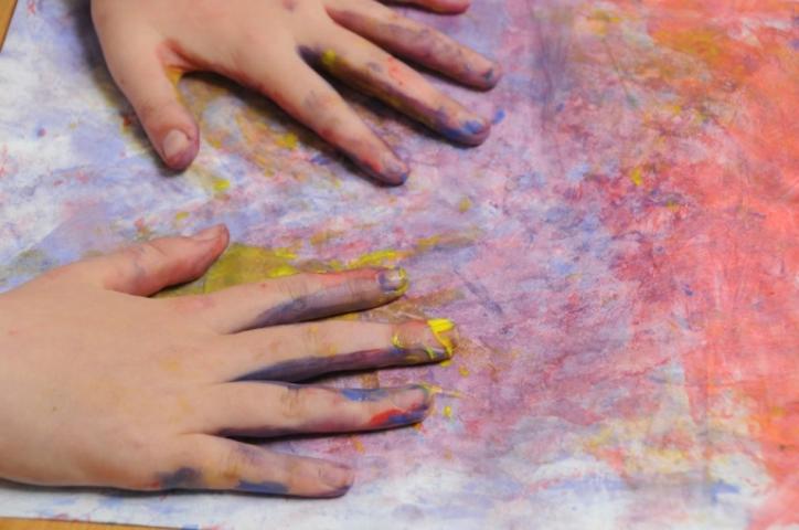 two childrens hands are covered in paint and are resting on a piece of paper that has been painted in blue, purple and pink