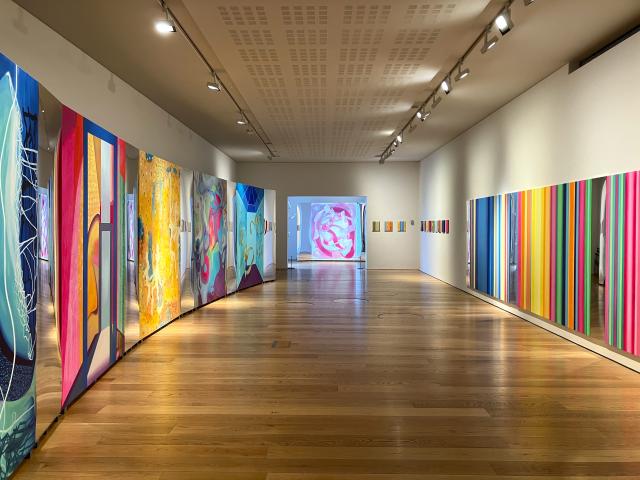 colourful abstract large paintings are on the walls of a long gallery room
