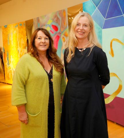 The artist Karen Ebbs is standing next to Christina Kennedy in from of large colourful abstract paintings