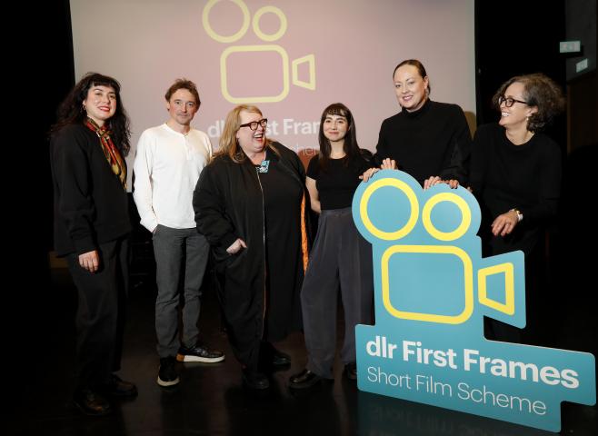 six people photographed on the stage in the Studio Theatre, dlr LexIcon. They are holding a bright blue cut out logo of dlr First Frames