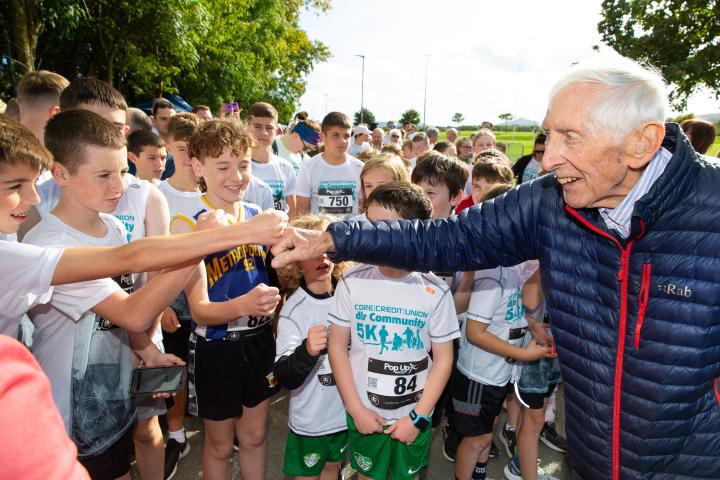 Ronnie Delaney at a community 5k run shaking hands with a group of children