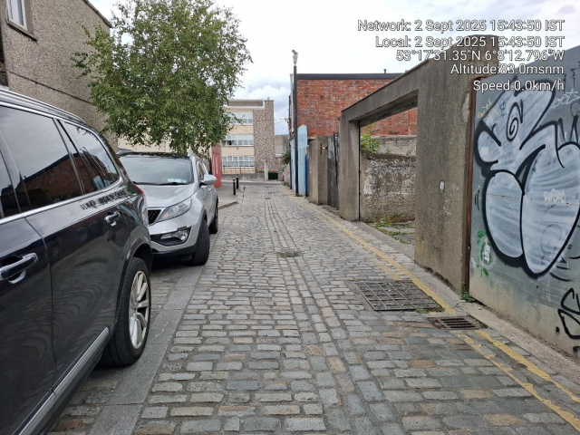 Street with parked cars and graffiti-covered wall.