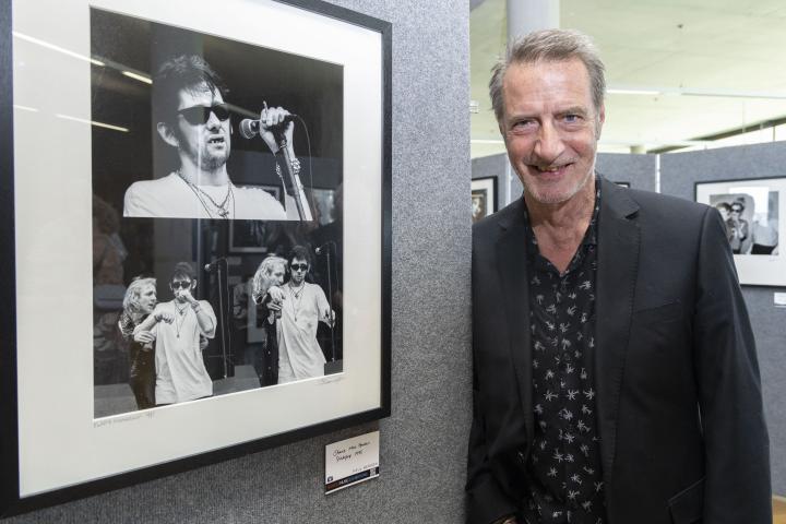 Paul Bergen stands with his three photographs of Shane McGowan from The Pogues singing with black sunglasses and a microphone.