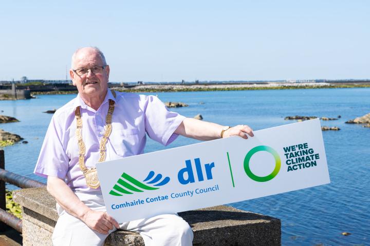 Cllr Jim Gildea, Cathaoirleach of Dún Laoghaire-Rathdown County Council sitting by the Dun Laoghaire Baths holding a plaque