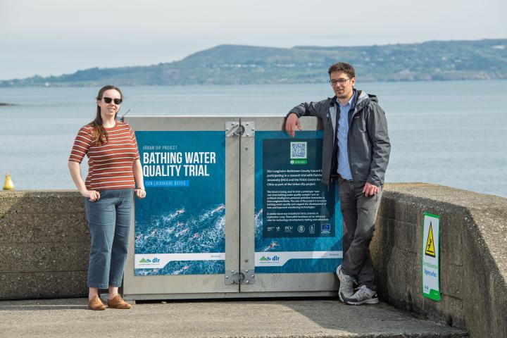 A man and woman standing at kiosk with sea in background