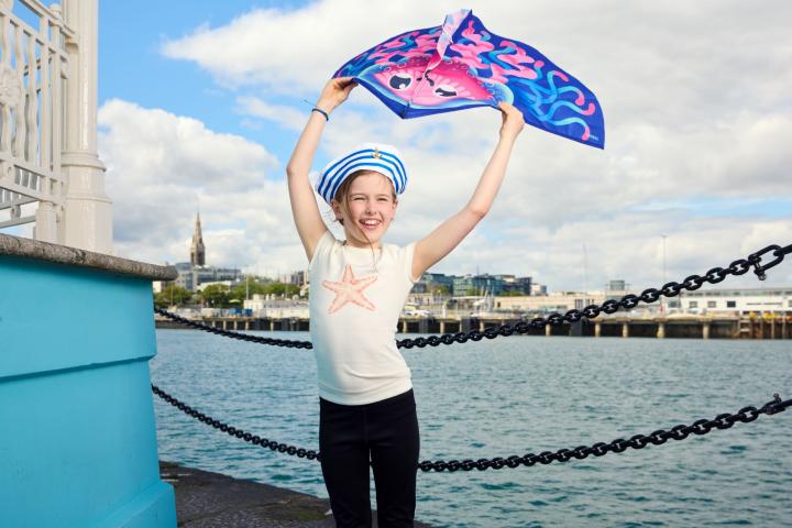 Girl standing beside sea holding a kite above her head
