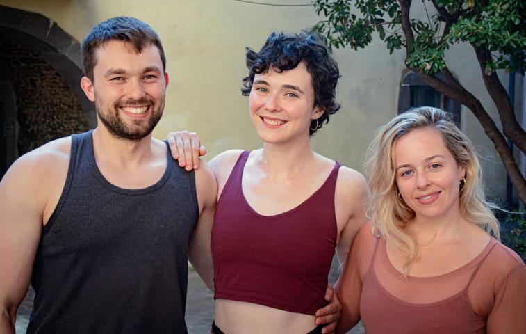 Photo of a man and two women standing with their arms around each others backs. They are all wearing exercise vests and are smiling at the camera