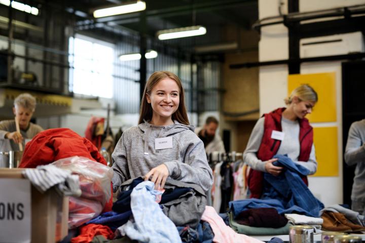 Volunteers sort and organise donated clothing on tables inside a community workspace, with piles of garments and supplies visible throughout the room.